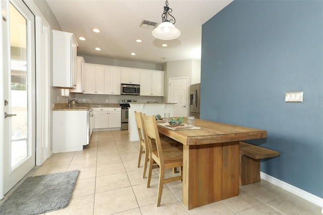 kitchen with appliances with stainless steel finishes, hanging light fixtures, a center island, light tile patterned floors, and white cabinets