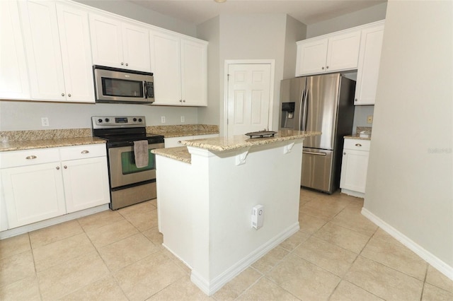 kitchen featuring appliances with stainless steel finishes, a center island, light stone countertops, light tile patterned floors, and white cabinets