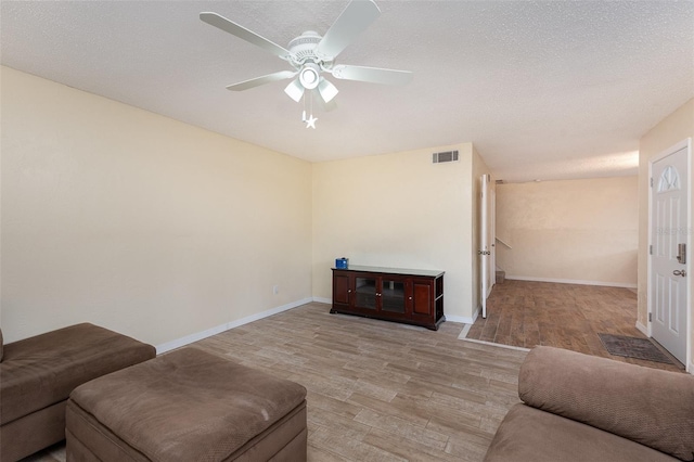 living room with a textured ceiling, ceiling fan, and light hardwood / wood-style flooring