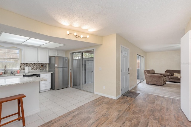 kitchen featuring tasteful backsplash, a healthy amount of sunlight, stainless steel fridge, and white cabinetry