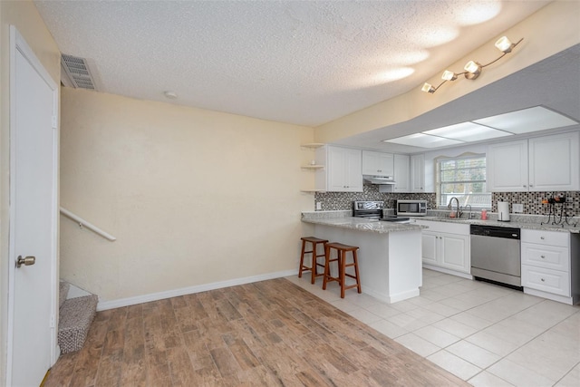 kitchen with kitchen peninsula, a kitchen bar, sink, appliances with stainless steel finishes, and white cabinets