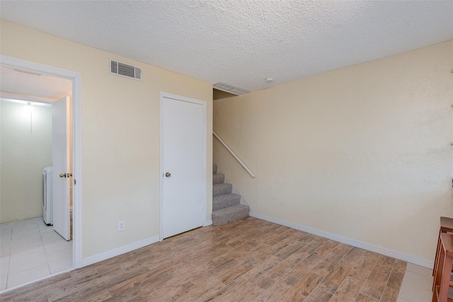 empty room with light wood-type flooring, a textured ceiling, and washer / clothes dryer