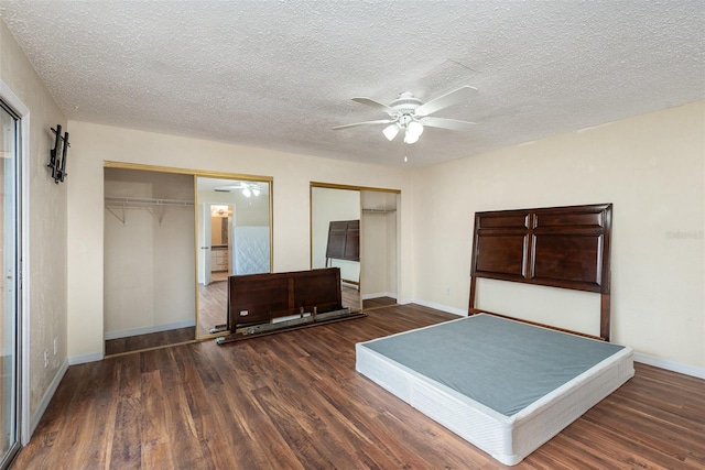 unfurnished bedroom featuring ceiling fan, two closets, a textured ceiling, and dark hardwood / wood-style flooring