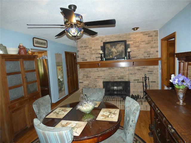 dining space featuring a fireplace, a textured ceiling, ceiling fan, and hardwood / wood-style floors