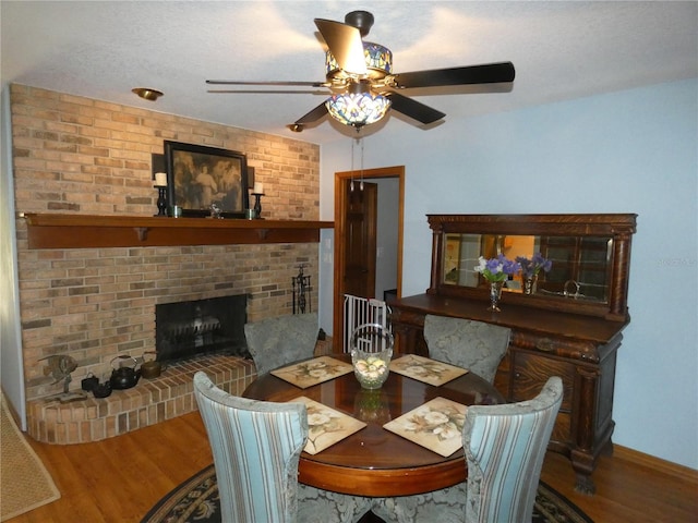 dining room featuring ceiling fan, a brick fireplace, a textured ceiling, and hardwood / wood-style flooring