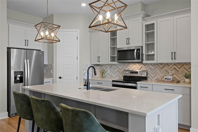 kitchen featuring appliances with stainless steel finishes, white cabinetry, sink, hanging light fixtures, and a kitchen island with sink