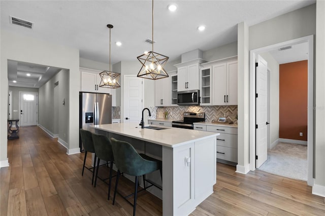 kitchen with sink, white cabinetry, appliances with stainless steel finishes, pendant lighting, and a kitchen island with sink