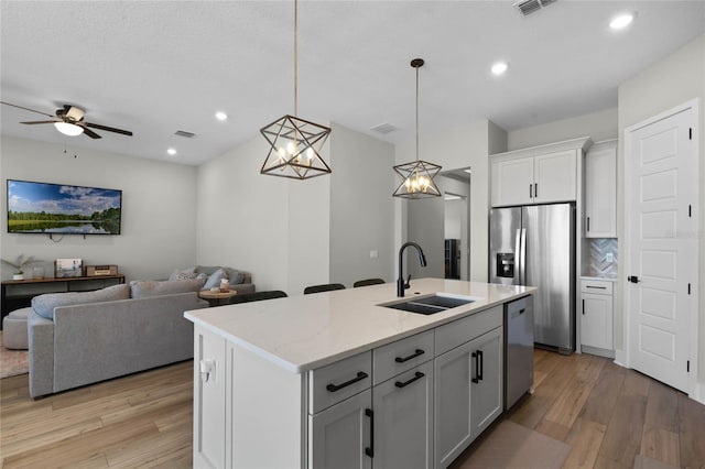 kitchen featuring a kitchen island with sink, sink, decorative light fixtures, and light stone countertops