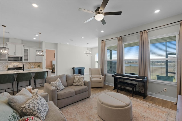 living room with ceiling fan with notable chandelier, light hardwood / wood-style flooring, plenty of natural light, and a water view