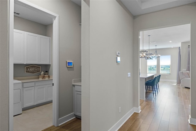 hallway with washer / clothes dryer, a chandelier, and light hardwood / wood-style flooring