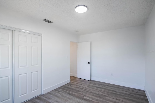 unfurnished bedroom featuring a textured ceiling, a closet, and wood-type flooring