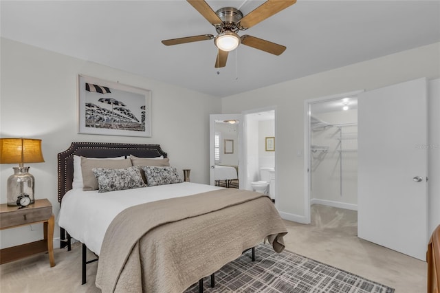 bedroom featuring a walk in closet, ensuite bathroom, light carpet, ceiling fan, and baseboards