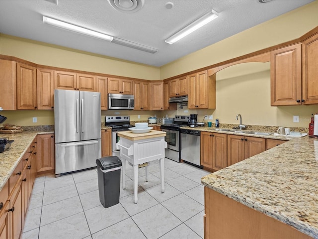 kitchen featuring light stone counters, light tile patterned floors, appliances with stainless steel finishes, a sink, and under cabinet range hood