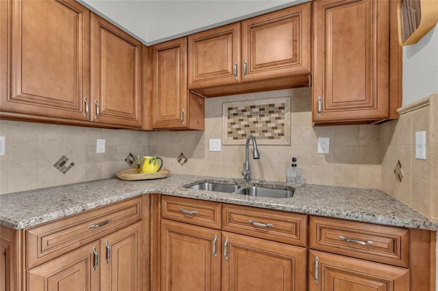 kitchen featuring brown cabinets, a sink, backsplash, and light stone countertops