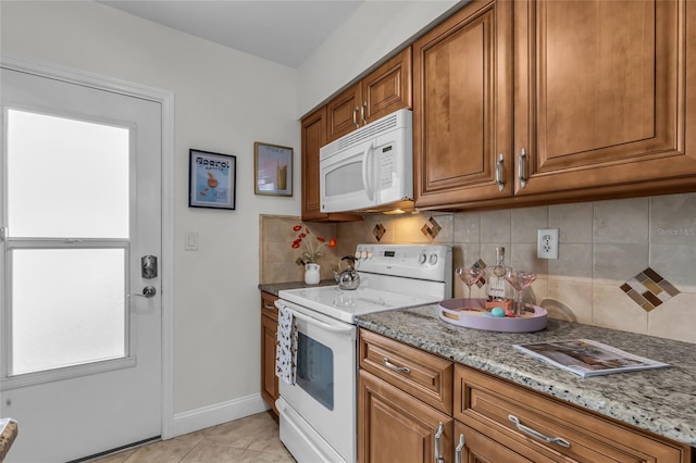 kitchen with light tile patterned floors, white appliances, brown cabinetry, and light stone countertops