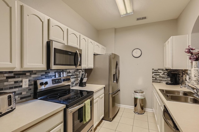 kitchen featuring stainless steel appliances, light tile patterned floors, sink, white cabinetry, and tasteful backsplash