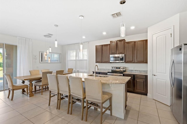 kitchen with hanging light fixtures, an island with sink, appliances with stainless steel finishes, and light tile patterned flooring