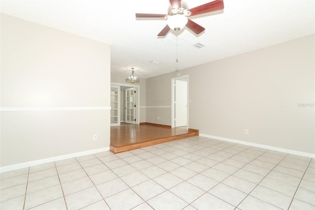 empty room with light tile patterned flooring and ceiling fan with notable chandelier