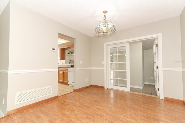 unfurnished room with sink, a textured ceiling, a notable chandelier, and light hardwood / wood-style flooring