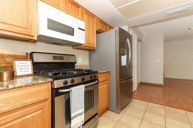 kitchen with backsplash, appliances with stainless steel finishes, light tile patterned flooring, and stone countertops