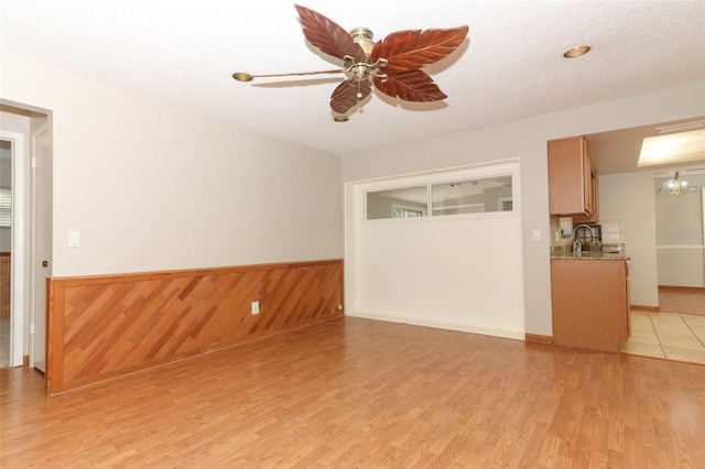 unfurnished living room with a textured ceiling, ceiling fan, light hardwood / wood-style floors, and sink