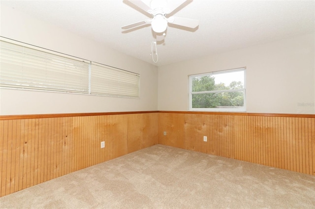 empty room featuring ceiling fan, wood walls, and carpet floors