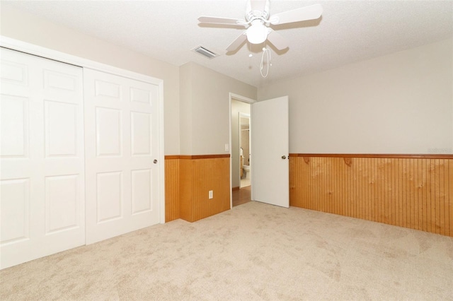 unfurnished bedroom featuring a closet, ceiling fan, wooden walls, carpet flooring, and a textured ceiling