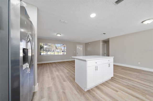 kitchen with a textured ceiling, a center island, white cabinetry, stainless steel fridge, and light hardwood / wood-style flooring