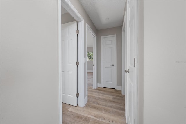 hallway with a textured ceiling and light wood-type flooring