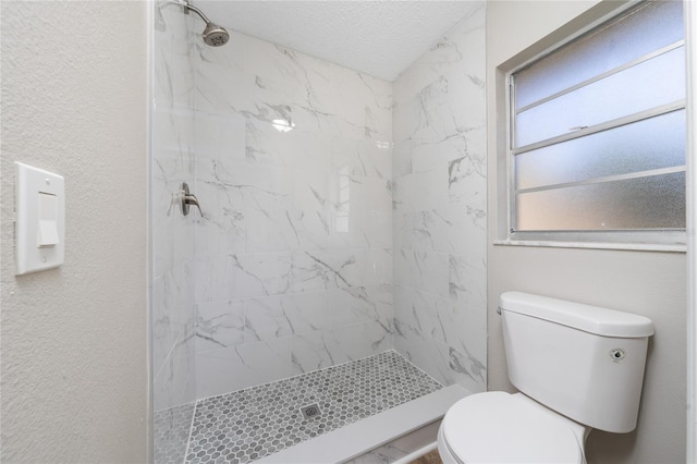 bathroom with a textured ceiling, toilet, and a tile shower