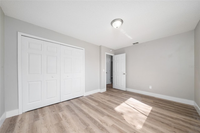 unfurnished bedroom with a textured ceiling, a closet, and light hardwood / wood-style flooring