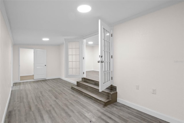 basement featuring french doors, crown molding, and light hardwood / wood-style flooring