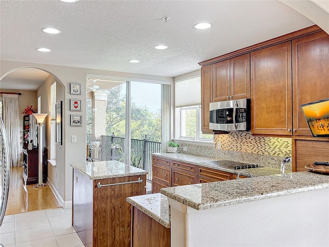 kitchen with light tile patterned floors, tasteful backsplash, light stone countertops, black electric cooktop, and kitchen peninsula