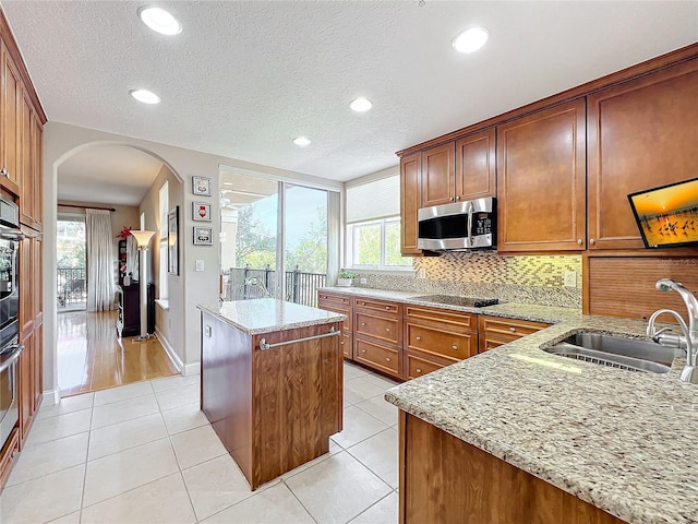 kitchen with light tile patterned flooring, light stone countertops, a center island, and sink