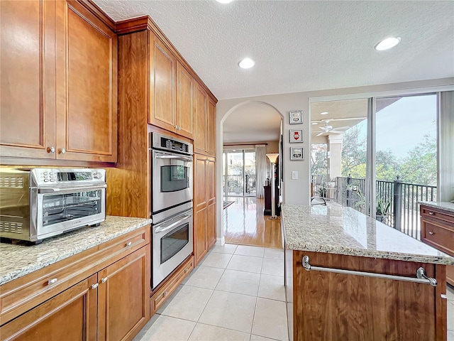 kitchen featuring a center island, a textured ceiling, light tile patterned floors, stainless steel double oven, and light stone countertops