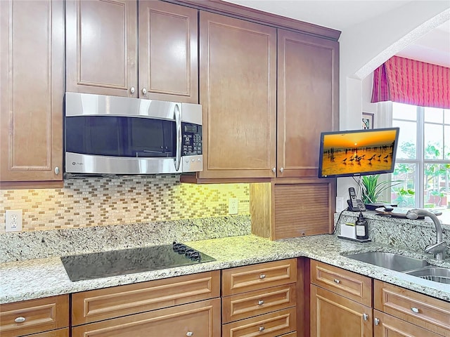 kitchen featuring black electric cooktop, light stone countertops, sink, and tasteful backsplash