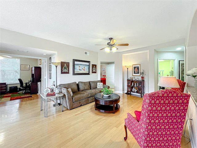 living room with ceiling fan, a textured ceiling, and light wood-type flooring