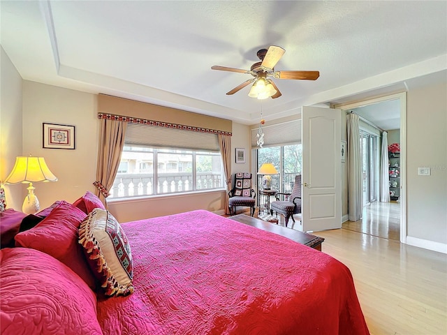 bedroom with a raised ceiling, ceiling fan, and light hardwood / wood-style floors