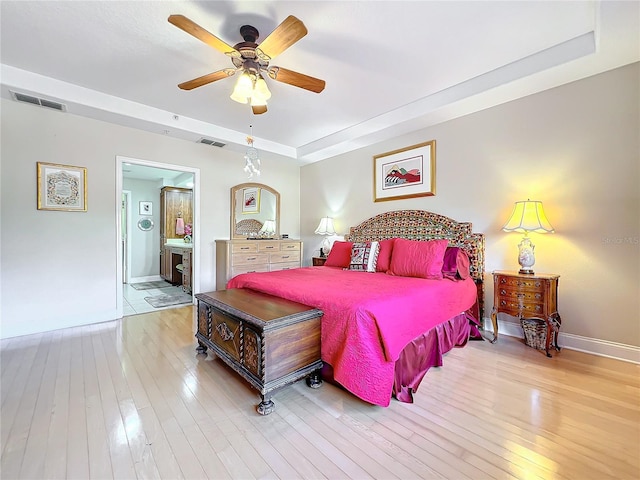 bedroom featuring a raised ceiling, connected bathroom, ceiling fan, and light hardwood / wood-style flooring