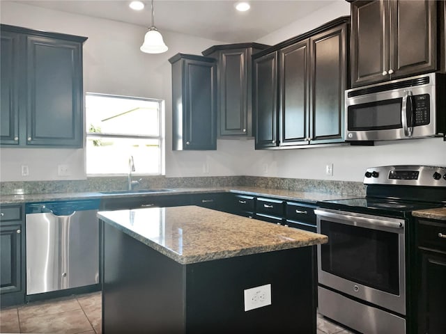 kitchen featuring stainless steel appliances, light stone counters, a kitchen island, sink, and decorative light fixtures