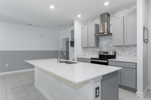 kitchen featuring sink, appliances with stainless steel finishes, gray cabinetry, a center island with sink, and wall chimney exhaust hood