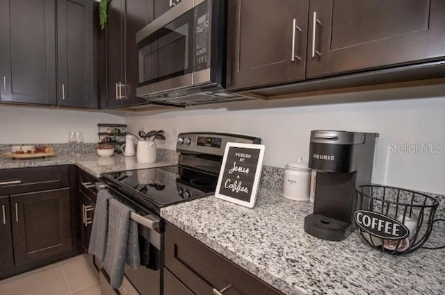 kitchen featuring stainless steel appliances, light tile patterned floors, dark brown cabinets, and light stone countertops