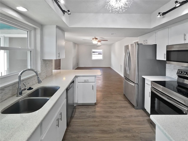 kitchen with stainless steel appliances, ceiling fan with notable chandelier, white cabinetry, and sink