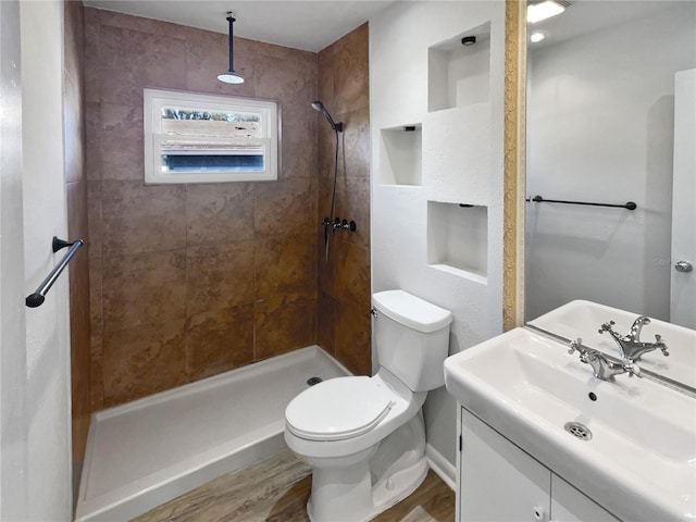 bathroom with toilet, a tile shower, wood-type flooring, and vanity