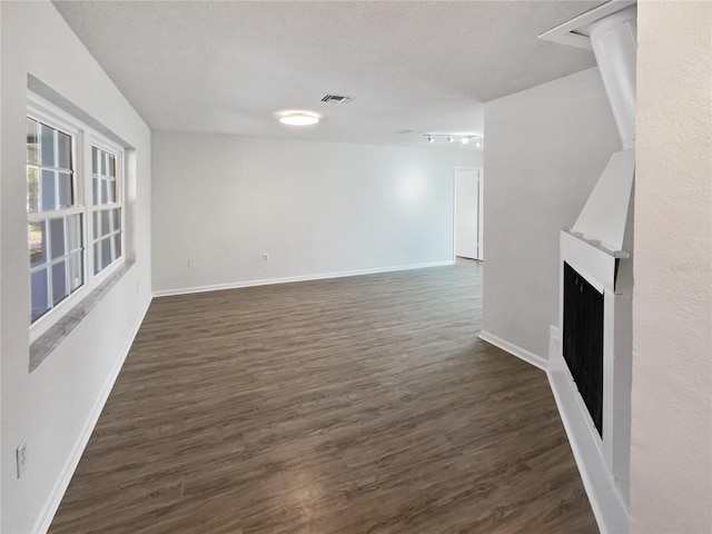 unfurnished living room with a textured ceiling, rail lighting, and dark hardwood / wood-style floors