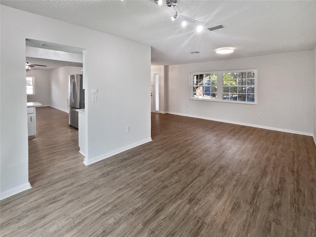 spare room featuring track lighting, a textured ceiling, ceiling fan, and dark wood-type flooring