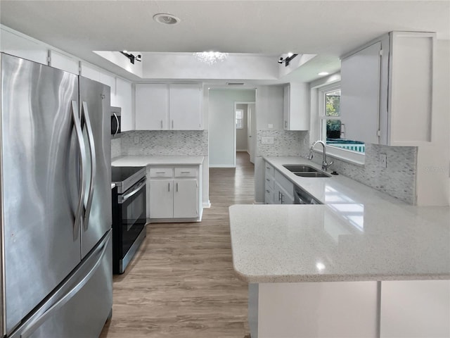 kitchen featuring white cabinets, stainless steel appliances, kitchen peninsula, and a tray ceiling