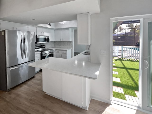 kitchen with stainless steel appliances, sink, white cabinetry, kitchen peninsula, and backsplash