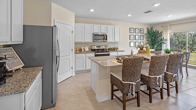 kitchen with light stone countertops, a center island with sink, light tile patterned floors, white cabinets, and appliances with stainless steel finishes