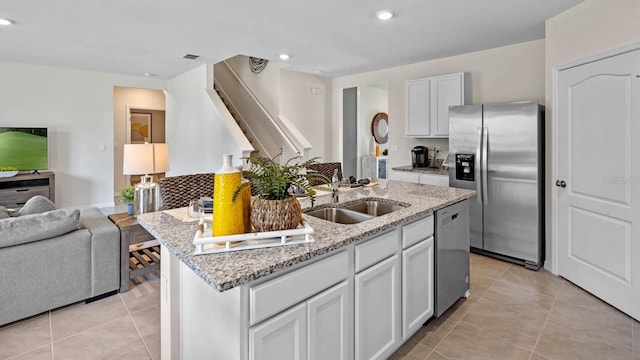 kitchen with a center island with sink, appliances with stainless steel finishes, light stone countertops, white cabinets, and sink